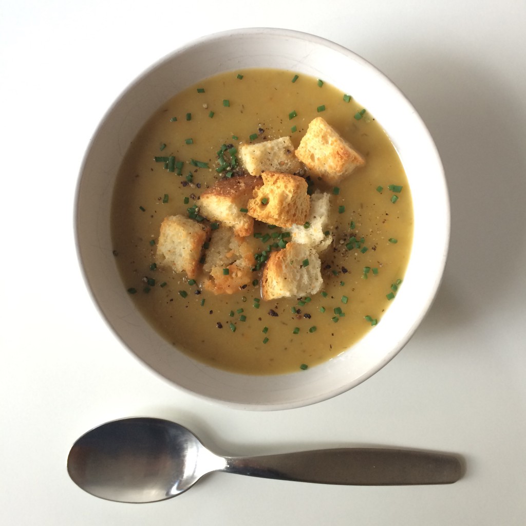 bowl of leek and potato soup with croutons, chives, and pepper. With spoon.